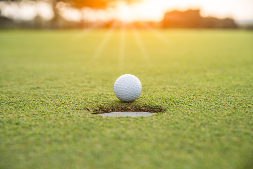 Golfista es poner la pelota de golf sobre verde hierba en el campo de golf para el juego con desenfoque de fondo y la luz solar ray photo
