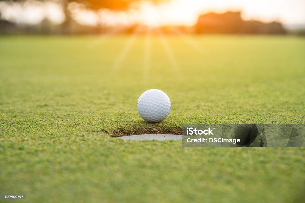 Golfer is putting golf ball on green grass at golf course for game with blur background and sunlight ray Golf Stock Photo