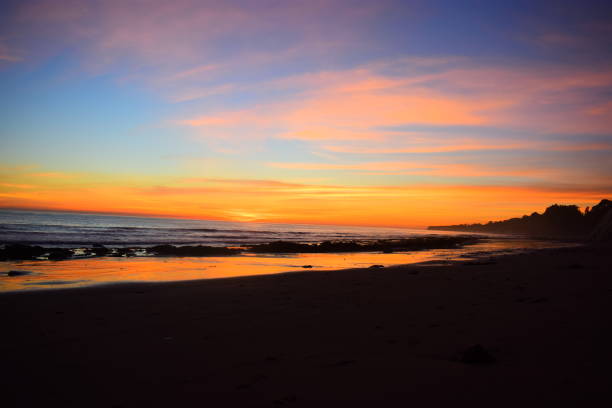 istock Orange clouds at sunset reflecting off wet sand. 1127904140