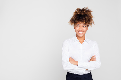 Portrait of beautiful young afro american businesswoman standing with her arms crossed on grey background with lots of space for your text.