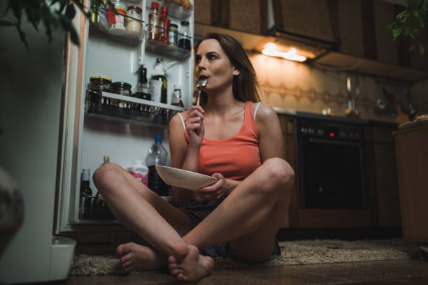 donna in cerca di spuntino di mezzanotte in frigorifero - ingordigia foto e immagini stock