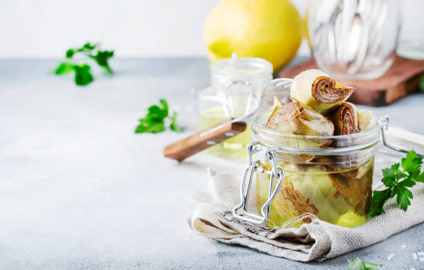 istock Canned artichokes in olive oil, in glass jar with fork, gray kitchen table 1127914276