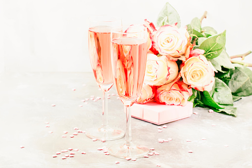 Love symbols - Bouquet of white and red roses, gift box, glasses with pink or rose champagne or sparkling wine for pair for St. Valentines Day, wedding, gray background, selective focus
