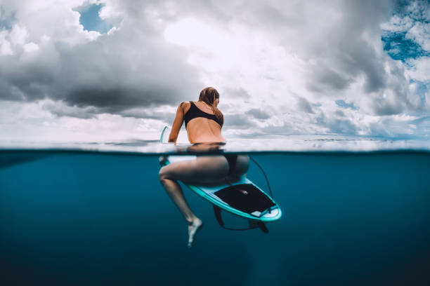 istock Surf girl sit at surfboard in blue ocean 1127914810