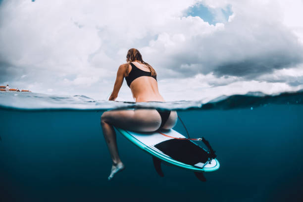 istock Surfer girl sit at surfboard in blue ocean 1127914866