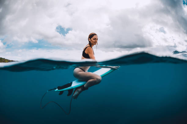 istock Attractive surf girl sit at surfboard in blue ocean 1127914870