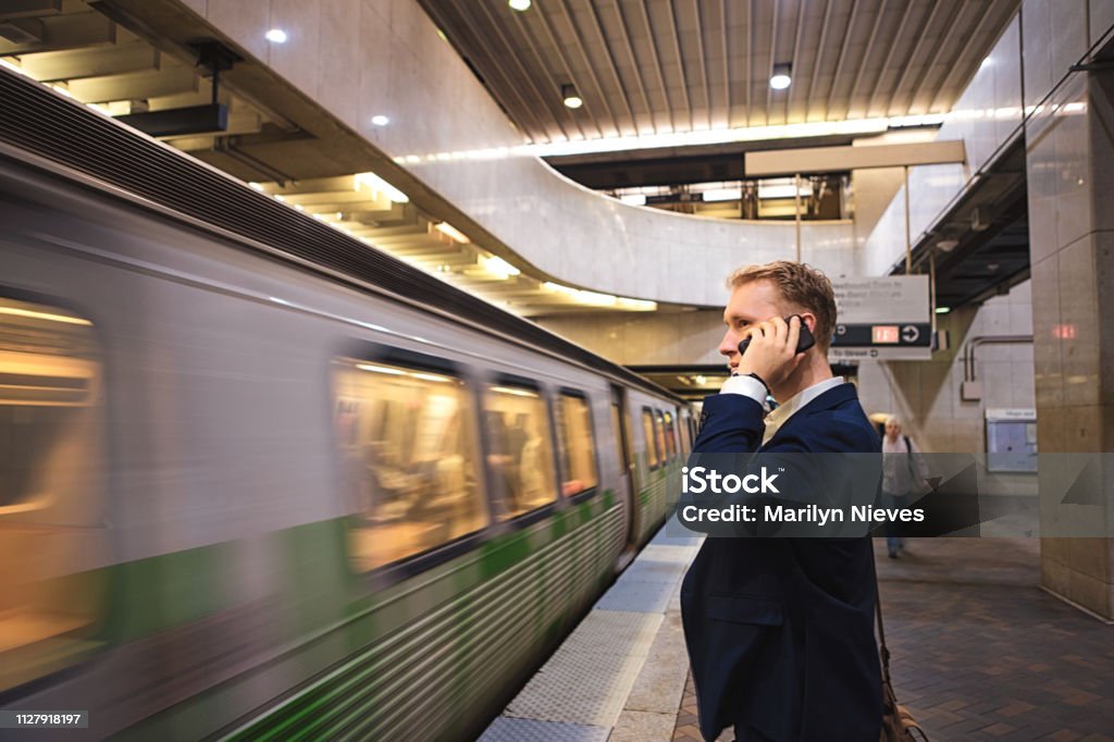 young adult businessman commuting to work using the phone as the train arrives at the subway station Adult Stock Photo