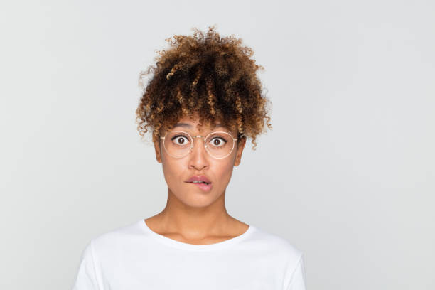 Nervous young african woman Close up portrait of young afro american woman looking nervous, biting her lips and looking at camera on gray background. Blush stock pictures, royalty-free photos & images