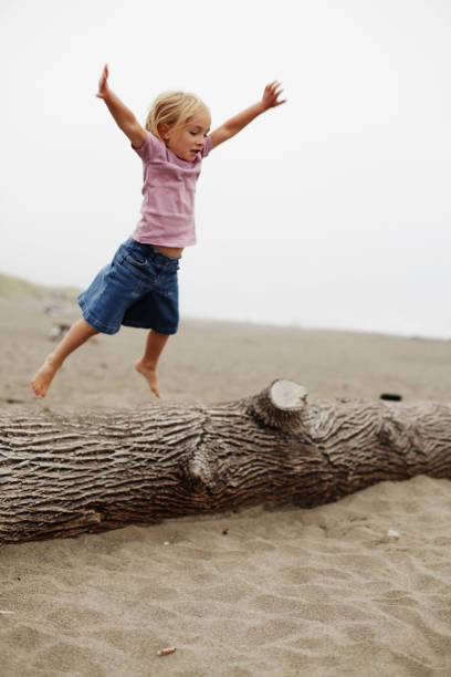 A little girl makes a big jump off a log into the sand on the beach