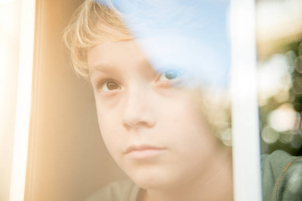 istock Close-Up Of Thoughtful Boy Looking Through Window 1127920956