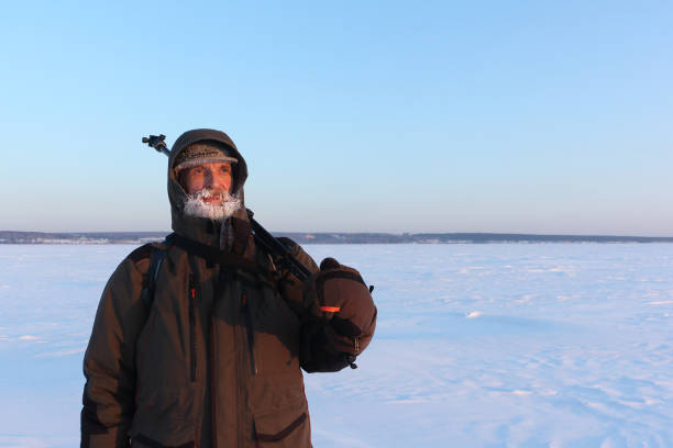 hombre con una barba congelada y un trípode al hombro en un fondo nevado en invierno al atardecer - only men senior men snow tripod fotografías e imágenes de stock