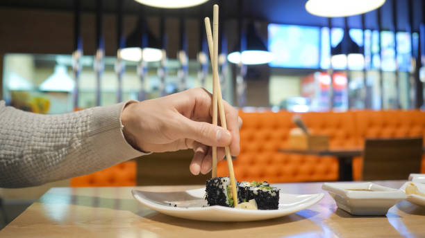 istock Young guy with chopsticks takes sushi from a plate in a japanese restaurant 1127927018