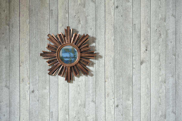 istock A small round mysterious antique mirror with a large frame in the form of outgoing rays. Mirror hanging on wood textured wallpaper background 1127932959