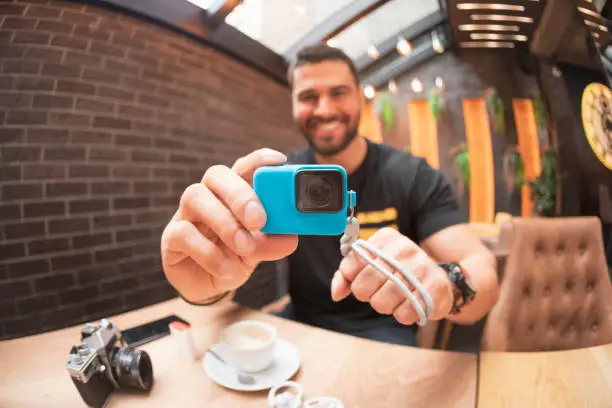 Handsome bearded man filming with action camera, using a GoPro  on coffee break in a  cafe restaurant  Freelance work
