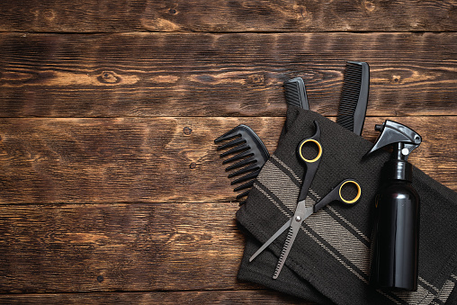 Hairdresser work table background with copy space. A various hairdressing tools such a hairbrushes, sprayer, towel and a scissors on a wooden board.
