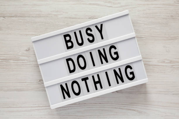 istock Modern board with text 'Busy doing nothing' on a white wooden surface, top view. From above, flat lay, overhead. Close-up. 1127949975