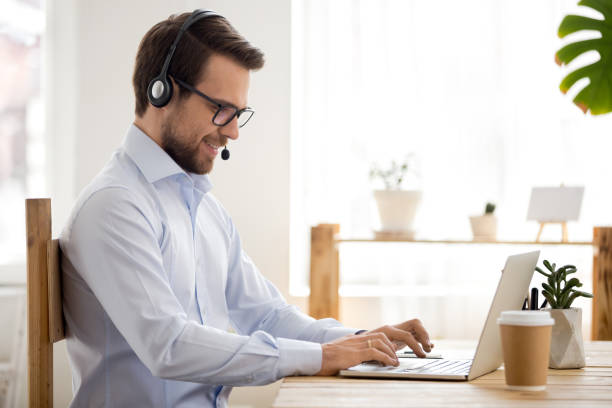 Smiling businessman in headset working on laptop make conference videocall