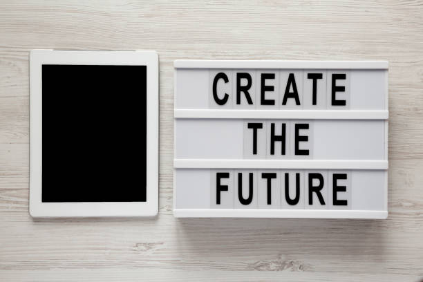 istock Top view, lightbox with text 'Create the future', tablet on a white wooden surface. From above, flat lay, overhead. 1127951083