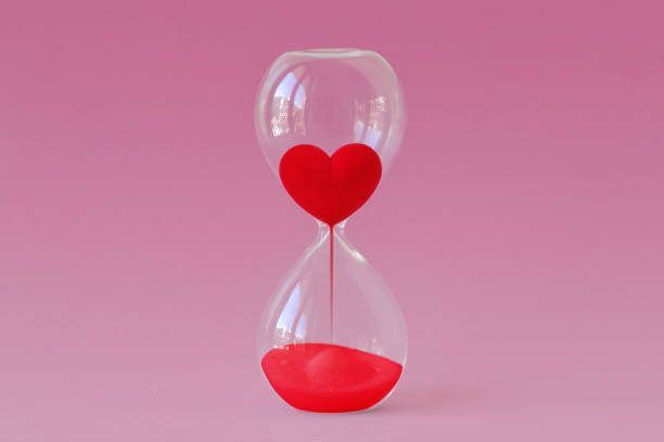 Red heart flowing in hourglass on pink background - Time for love concept stock photo