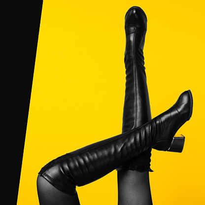 Sexy legs wearing black leather boots on yellow background - Image