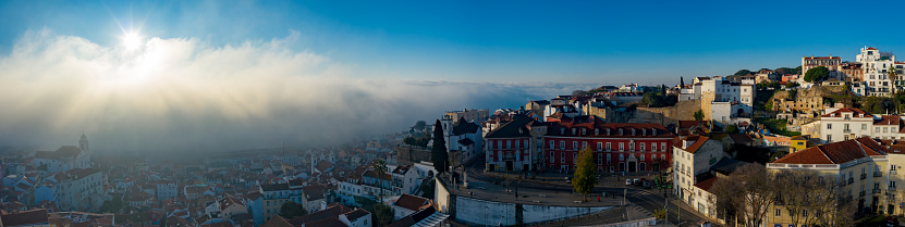 Aerial; misty morning in the ancient Alfama district of the Portuguese capital; drone view of pretty little houses, sun rising up over the clouds; natural phenomen; unusual weather in touristic area