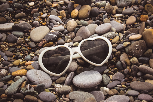 White sunglasses in the shape of a heart lie on the seashore