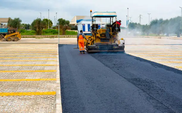 Photo of Asphalt paver with asphalt heated to temperatures above 160 ° during road at the construction. Road specialized equipment is laying the way.