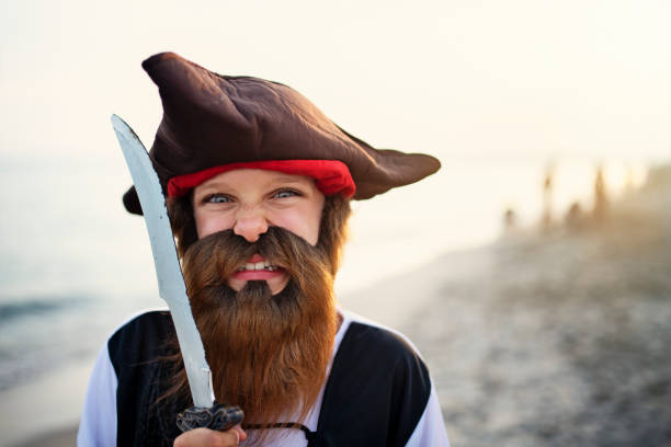 Boy wears pirate costume with eye patch and hat and steering sailboat