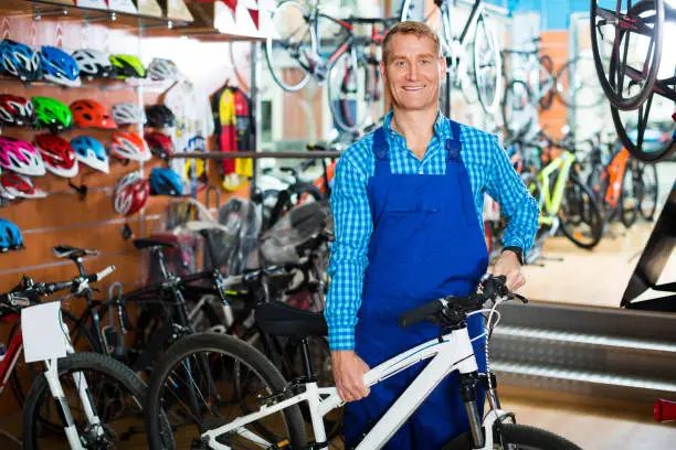 cheerful smiling man seller wearing uniform standing in bike store