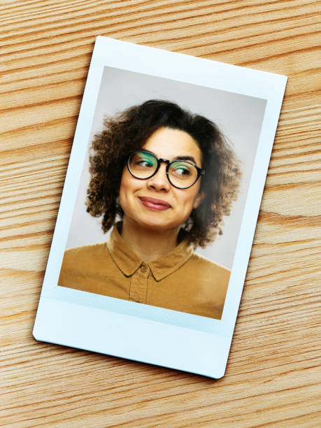 Printed portrait of young happy woman from instant camera looking away. Printed portrait of young hispanic happy woman from instant camera looking to the side. (Fuji Instax film). Vertical shot of hispanic real people smiling with long curly hair and glasses. Photography from a DSLR camera. Sharp focus on printed photo. instant camera photos stock pictures, royalty-free photos & images