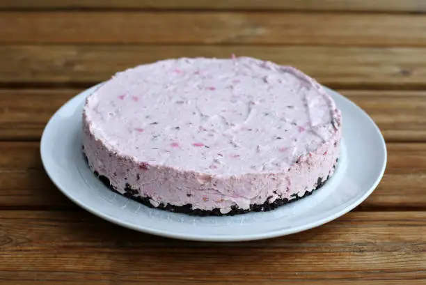 Homemade raspberry-cookie-chocolate moussecake. Delicious cake with brown chocolatey base and pink mousse on top of it. Photographed on a white table.