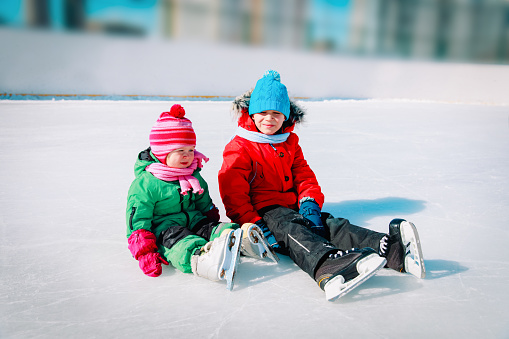 happy little boy and girl skating together in winter snow