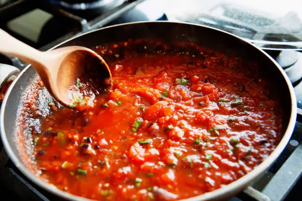 Vilnius, Lithuania - June 17, 2011: preparing of a homemade tomato sauce in a frying pan from fresh tomatoes.