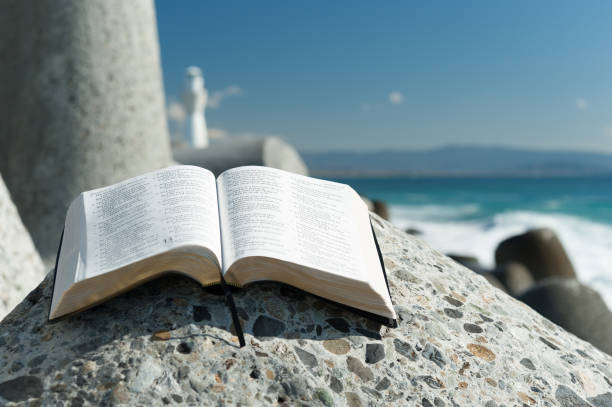 istock Open Bible on a big stone on a beautiful day with blue sky and few clouds. Close-up. 1127974884