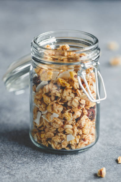 szklany słoik organicznej granoli z jagodami, frytkami z orzechów kokopłetnych i nasionami na niebieskim stole kuchennym. - jar oatmeal granola glass zdjęcia i obrazy z banku zdjęć