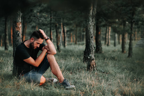 istock Young depressed man sitting alone in the forest 1127975721