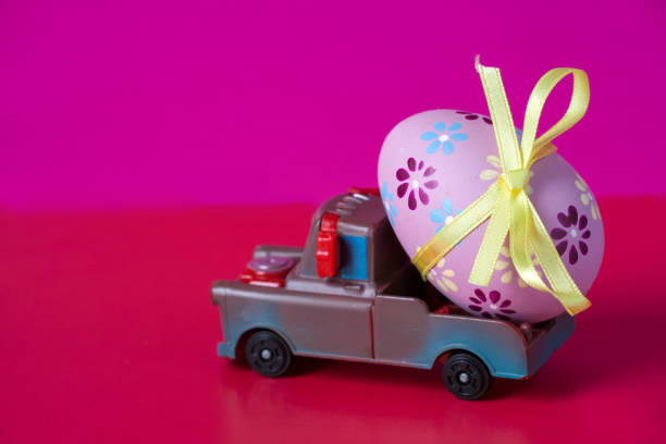 istock Pickup toy carrying one decorated easter egg on a pink background. 1127977067