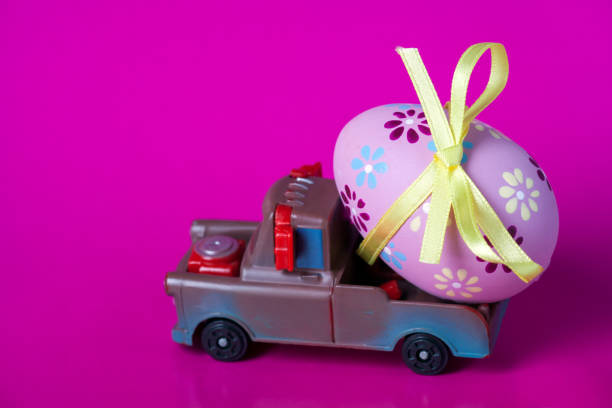 istock Pickup toy carrying one decorated easter egg on a pink background. 1127977068