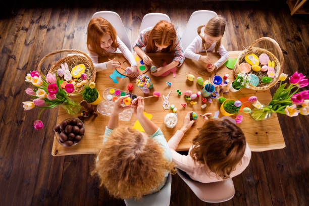 istock Close up top above high angle view photo three children mom granny make decorate eggs easter symbols weekend children day concept pretty cute ready celebrate holiday sit big wooden table floor 1127982804