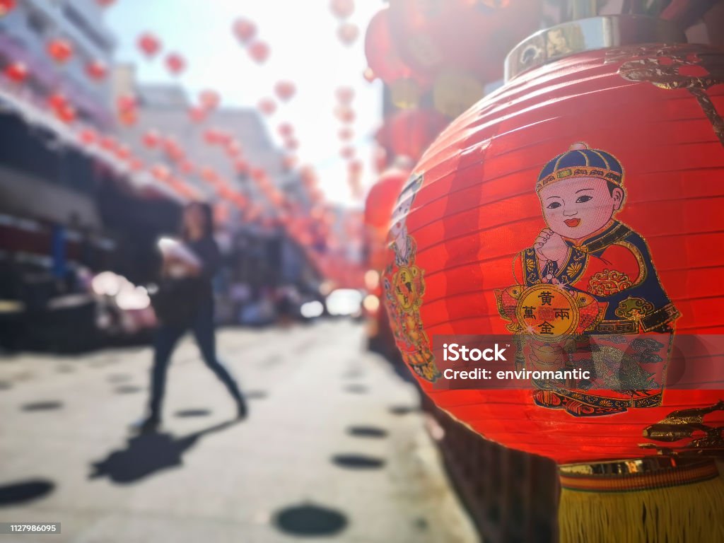 Colorful Chinese New Year red and gold traditional festival lanterns adorn part of the famous traditional Chiang Mai Worawot Market near the river in downtown Chiang Mai, whilst tourists and locals pass through the street admiring the decorations. Abstract Stock Photo