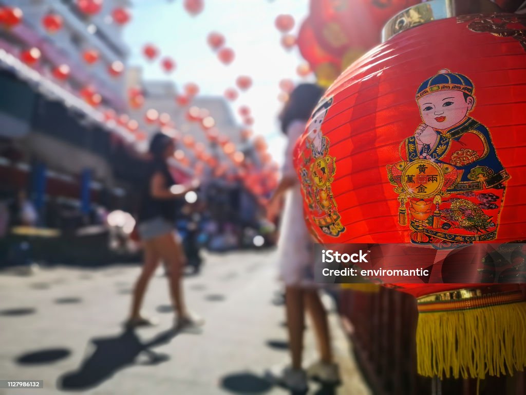 Colorful Chinese New Year red and gold traditional festival lanterns adorn part of the famous traditional Chiang Mai Worawot Market near the river in downtown Chiang Mai, whilst tourists and locals pass through the street admiring the decorations. Abstract Stock Photo