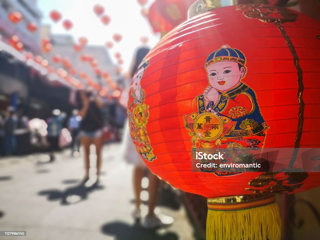 Colorful Chinese New Year red and gold traditional festival lanterns adorn part of the famous traditional Chiang Mai Worawot Market near the river in downtown Chiang Mai, whilst tourists and locals pass through the street admiring the decorations. Abstract Stock Photo