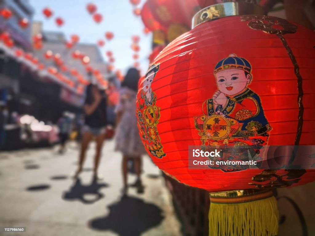 Colorful Chinese New Year red and gold traditional festival lanterns adorn part of the famous traditional Chiang Mai Worawot Market near the river in downtown Chiang Mai, whilst tourists and locals pass through the street admiring the decorations. Abstract Stock Photo