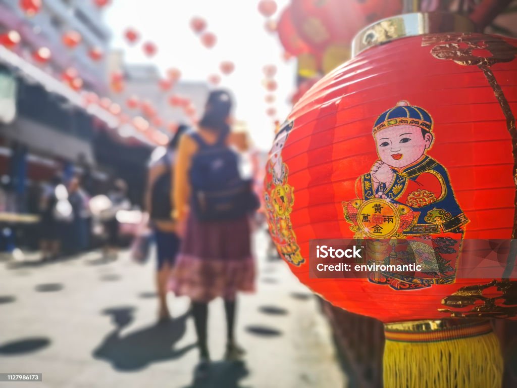 Colorful Chinese New Year red and gold traditional festival lanterns adorn part of the famous traditional Chiang Mai Worawot Market near the river in downtown Chiang Mai, whilst tourists and locals pass through the street admiring the decorations. Abstract Stock Photo