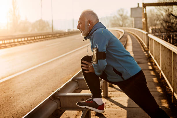 Senior man warming up for jogging on a city bridge stock photo
