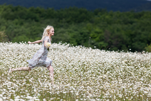 Attractive young woman skips along camomile field in overcast day