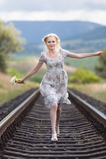 istock Slim girl in light dress runs along railway 1127998105