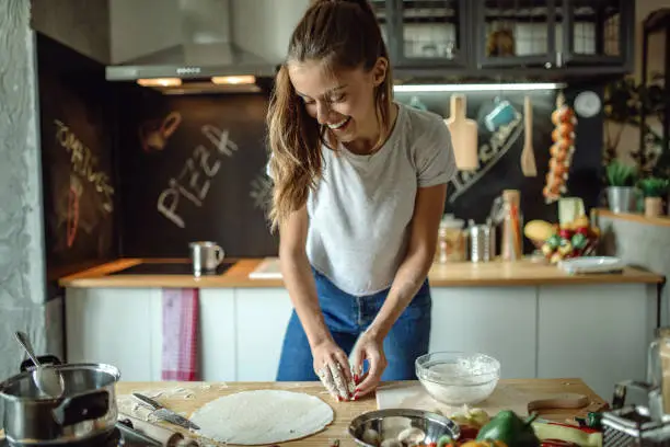 Woman in kitchen preparing dough for pizza