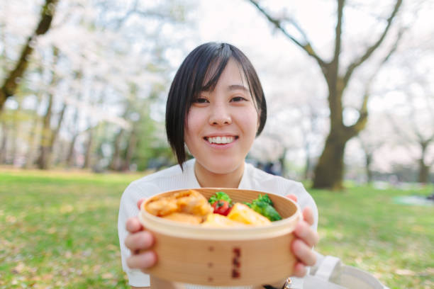 A young Japanese woman is having a picnic in spring time under cherry trees.