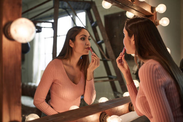 istock Woman applying lip gloss while looking at mirror 1128017184